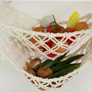 Overhead view of a two-tiered macrame fruit hammock filled with fresh bananas, tomatoes, and apples, showcasing the detailed knotwork, providing a stylish and bohemian kitchen storage solution