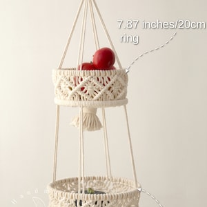 Elegant cream-colored macrame two-tier fruit basket, with dimensions labeled, showcasing vegetables in a bright, natural setting. Handmade craftsmanship by Macramebeautiful