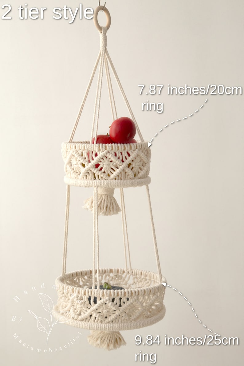 Elegant cream-colored macrame two-tier fruit basket, with dimensions labeled, showcasing vegetables in a bright, natural setting. Handmade craftsmanship by Macramebeautiful