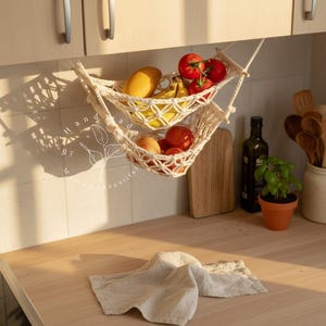 Handmade macramé two-tier fruit hammock in natural cotton, hanging kitchen fruit basket with apples, oranges and kiwis — boho farmhouse decor, space-saving organizer for countertop or wall.