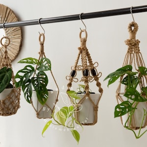 Handcrafted jute macramé plant hangers with wooden rings, featuring four distinct knot patterns suspending white ceramic pots filled with lush green pothos and monstera vines—boho-chic indoor décor perfect for hanging planters, windowsills, balconies.