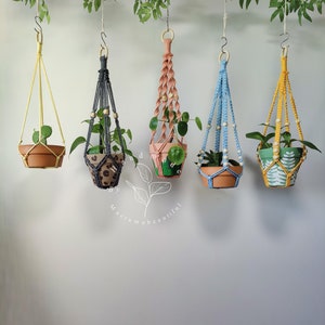 Macrame plant hangers in a range of bold colors, each intricately woven and embellished with beads, created by Macramebeautiful, showcasing potted greenery in a botanical setting