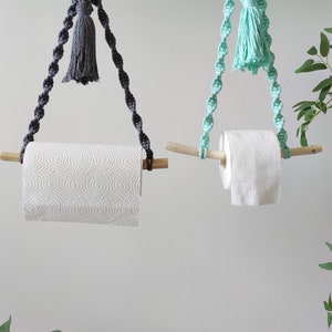 K&ouml;nnte beinhalten: Zwei Makramee-Papierhandtuchhalter mit Holzstiften und Quasten. Ein Halter hat eine graue Quaste und der andere eine hellblaue Quaste.