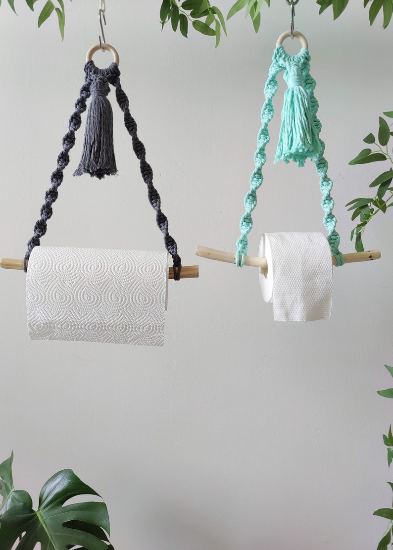 K&ouml;nnte beinhalten: Zwei Makramee-Papierhandtuchhalter mit Holzstiften und Quasten. Ein Halter hat eine graue Quaste und der andere eine hellblaue Quaste.