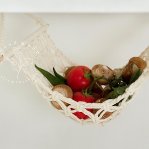 A close-up of a macrame fruit hammock cradling a vibrant selection of tomatoes and mushrooms, featuring intricate knotting patterns, perfect for a minimalist kitchen aesthetic