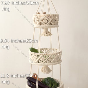 Elegant cream-colored macrame three-tier fruit basket, with dimensions labeled, showcasing vegetables in a bright, natural setting. Handmade craftsmanship by Macramebeautiful