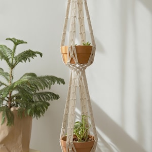 Handcrafted macrame plant hanger showcasing two suspended pots with intricate knotwork detail, set against a minimalist background to emphasize its delicate design and craftsmanship.