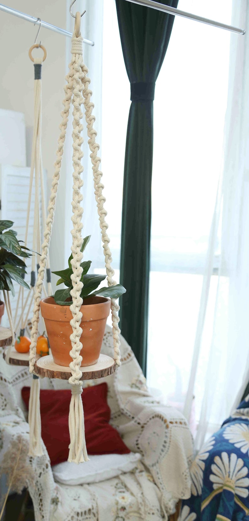 May include: A white macrame plant hanger with a terracotta pot and green plant hanging from it. The hanger is attached to a wooden dowel rod and has tassels at the bottom.