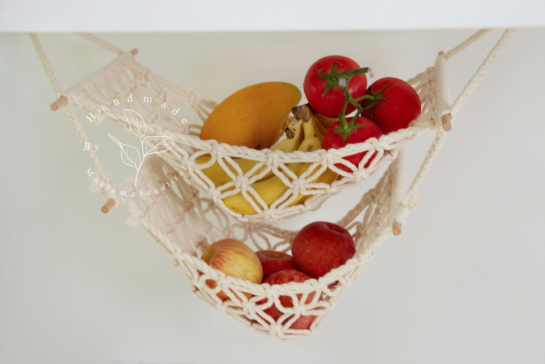 Overhead view of a two-tiered macrame fruit hammock filled with fresh bananas, tomatoes, and apples, showcasing the detailed knotwork, providing a stylish and bohemian kitchen storage solution