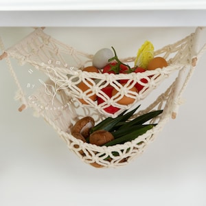Overhead view of a two-tiered macrame fruit hammock filled with fresh bananas, tomatoes, and apples, showcasing the detailed knotwork, providing a stylish and bohemian kitchen storage solution