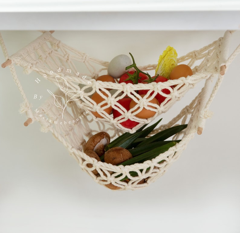 Overhead view of a two-tiered macrame fruit hammock filled with fresh bananas, tomatoes, and apples, showcasing the detailed knotwork, providing a stylish and bohemian kitchen storage solution