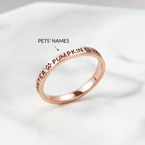 Peut inclure: Une bague en or rose gravée des mots "BAXTER PUMPKIN HALO" autour de la bande. La bague présente également des empreintes de pattes entre les noms.