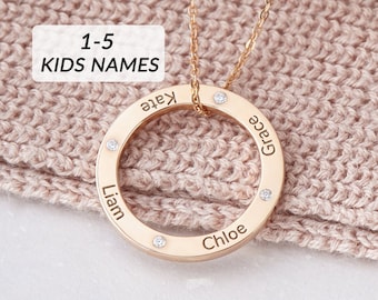 May include: Gold necklace with a circular pendant that has the names "Liam", "Chloe", "Kate", and "Grace" engraved around the edge. The pendant is accented with small clear stones.
