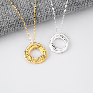 May include: Two personalised necklaces with interlocking rings. One is gold-toned, the other silver-toned. Each ring is engraved with names. The gold necklace has the names "RACHEL", "JOE", "MASON", "LYDIA", and "SEVANA". The silver necklace has the names "BRETT" and "GRANT".