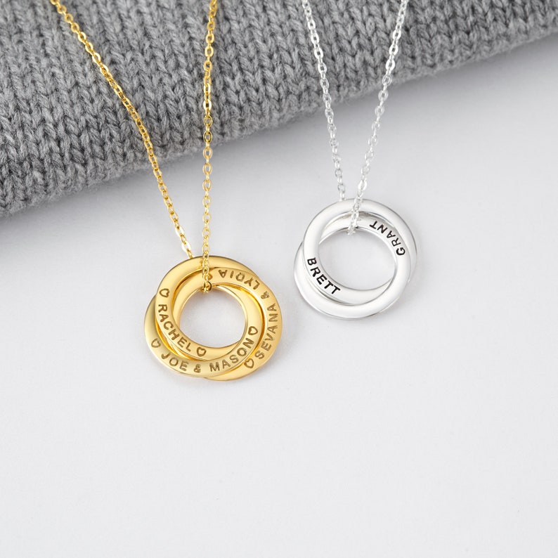 May include: Two personalised necklaces with interlocking rings. One is gold-toned, the other silver-toned. Each ring is engraved with names. The gold necklace has the names "RACHEL", "JOE", "MASON", "LYDIA", and "SEVANA". The silver necklace has the names "BRETT" and "GRANT".