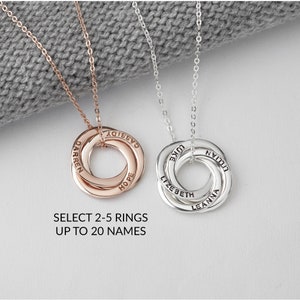 May include: Two personalised necklaces with interlocking rings. One is rose gold, the other silver. Each ring is engraved with names. The text below reads: SELECT 2-5 RINGS UP TO 20 NAMES.
