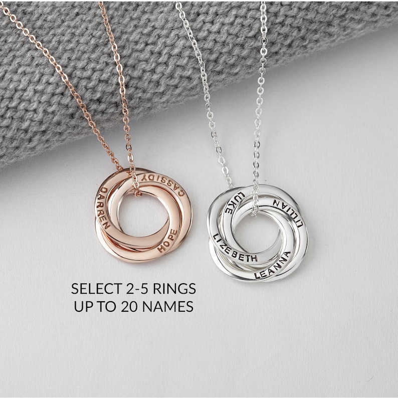 May include: Two personalised necklaces with interlocking rings. One is rose gold, the other silver. Each ring is engraved with names. The text below reads: SELECT 2-5 RINGS UP TO 20 NAMES.