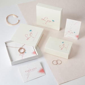 May include: A rose gold jewellery set, including a necklace, bracelet, and rings, presented with gift boxes and cards. The boxes and cards display a logo with the text "Love You Millions". The background is a soft pink and white.
