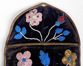 May include: A dark purple velvet pouch featuring intricate beadwork in the shape of flowers and leaves. The design includes pink, blue, and gold beads arranged in floral patterns with white beaded stems, all bordered by a brown fabric trim.