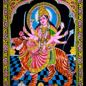 May include: A colorful tapestry depicting a Hindu goddess with multiple arms riding a tiger. The goddess is adorned with jewelry and flowers, and the tiger is depicted in a vibrant orange and black pattern.