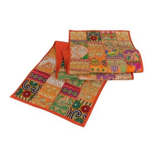Puede incluir: Un camino de mesa rectangular con un diseño de retazos de varios cuadrados de tela bordados en tonos vibrantes de naranja, verde, rosa y dorado. El textil muestra intrincados patrones florales y geométricos con detalles de hilo metálico.