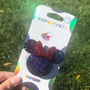May include: A black and red glitter PopSocket phone grip with a Minnie Mouse design. The PopSocket is packaged on a white card with the PopSockets logo and the text "PopGrip".