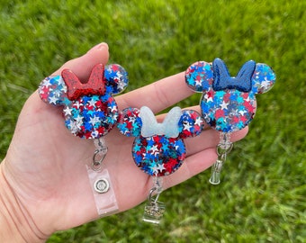 May include: Three red, white, and blue glitter Mickey Mouse head shaped retractable badge holders with a star pattern.