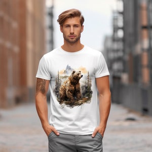 May include: A white t-shirt with a brown bear illustration. The bear is standing on a log in a forest setting with a mountain in the background. The illustration is done in a watercolor style.