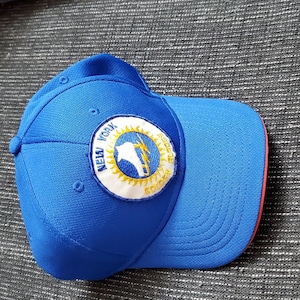 Op de afbeelding: Blauwe baseballpet met een geel en wit embleem met de tekst "New York City Soccer 2002".