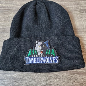 May include: Black knitted beanie with a Minnesota Timberwolves logo patch. The logo features a wolf's head with green trees and the team name in blue.