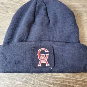 May include: A navy blue knit beanie with a red and white felt patch that says "GA" in a stylized font.