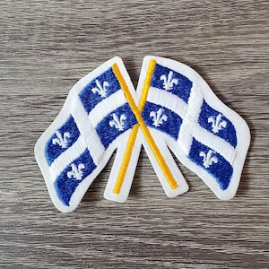 Puede incluir: Dos parches de tela blanca con banderas azules y blancas de Fleur-de-lis cosidas sobre ellos. Las banderas están cruzadas y tienen costuras amarillas.