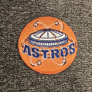 May include: Orange and blue embroidered patch featuring a baseball stadium and the word "ASTROS" in a circular design.