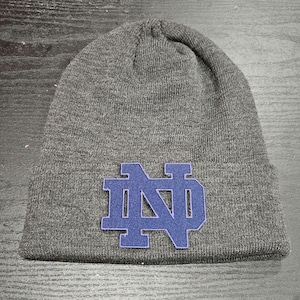 May include: Gray knitted beanie with a blue felt Notre Dame logo.