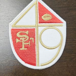 Peut inclure: Un écusson brodé blanc et rouge avec un contour doré. L'écusson représente un ballon de football, les lettres "SF" et le chiffre "9".