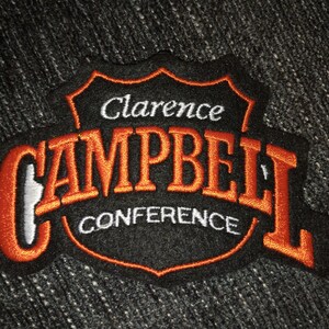 May include: Orange and white embroidered patch with the text "Clarence Campbell Conference" on a black background.