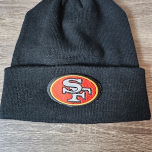 May include: Black knit beanie with a red, yellow, and white embroidered patch that says "SF" on it.