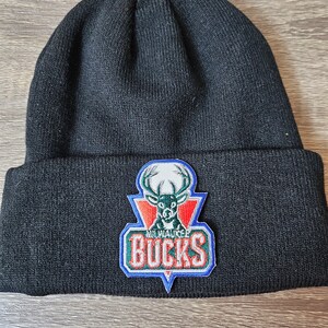 May include: Black knit beanie with a green, red and blue Milwaukee Bucks logo patch featuring a deer with antlers.