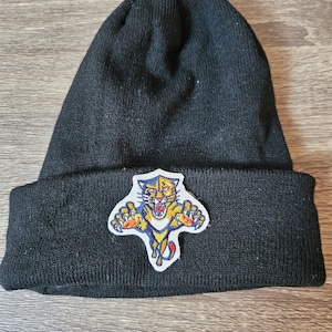 Peut inclure: Bonnet noir en tricot avec un logo de couguar brodé en jaune, bleu et rouge.