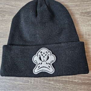 Op de afbeelding: Zwarte beanie met een grijs geborduurd eendengezicht aan de voorkant.