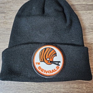 Puede incluir: Gorro de punto negro con un parche bordado blanco y naranja que representa un casco de fútbol y el texto "TM BENGALS".