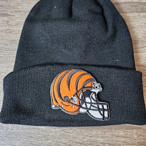 Puede incluir: Gorro de punto negro con un logotipo bordado de casco de Cincinnati Bengals en negro, naranja y blanco.
