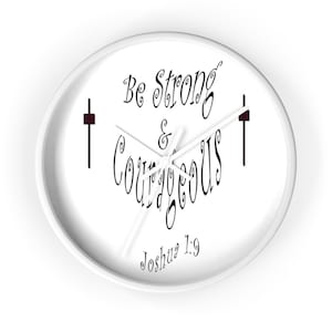 May include: White round clock with black hands and black text that reads "Be Strong & Courageous Joshua 1:9". There are two black crosses on either side of the text.