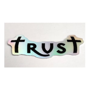 May include: A holographic sticker with the word "TRUST" in black letters with a cross on either side of the word.
