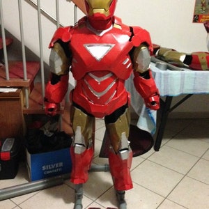 Può includere: Un costume di Iron Man rosso e oro con un elmetto e una placca toracica rossa. Il costume è in piedi su una piattaforma fatta di tubi in PVC. Il costume è fatto di schiuma e dipinto di rosso e oro.
