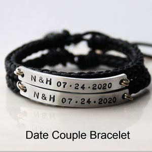 May include: A pair of black braided cord bracelets with silver metal plates engraved with the text "N & H 07.24.2020". The bracelets are a matching couple's set.