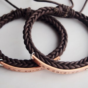 May include: Two brown braided rope bracelets with copper plates engraved with the text "K & G 28.9.22".