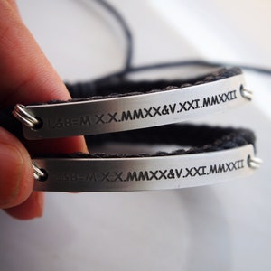 May include: Two black braided bracelets with silver metal plates engraved with the text "L&B=M X.X.MMXX&V.XXI.MMXXII".