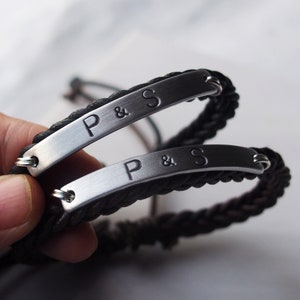 May include: Two black braided cord bracelets with silver metal plates engraved with "P & S".