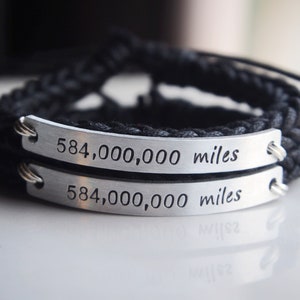 May include: Two black braided bracelets with silver metal tags that read "584,000,000 miles".